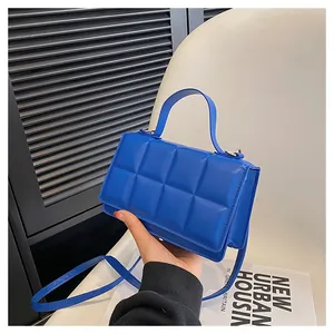 Détail d'un sac à bandoulière matelassé bleu avec ferrures dorées et poignée lisse