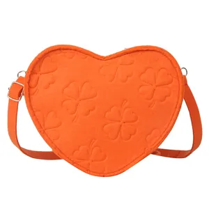 Bright orange heart-shaped crossbody bag with embossed clover patterns and adjustable strap
