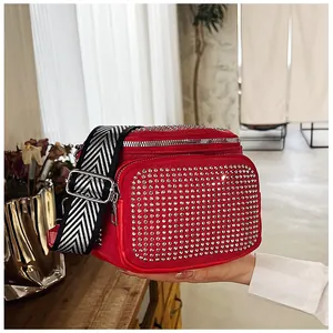 Détail d'un sac bandoulière rouge avec strass et sangle rayée noire et blanche