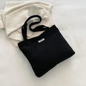 Close-up of black corduroy tote bag featuring a white Fashion label and double straps