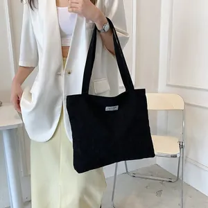 Detailed view of black corduroy tote bag featuring a minimalist white fashion label