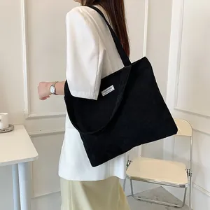 Side view of a black corduroy tote bag with Fashion label worn by a model