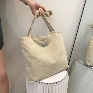 Close-up of beige corduroy tote bag showing vertical rib texture and FASHION label