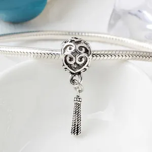 Detailed close-up of antique silver heart bead with hollow scroll patterns and tassel