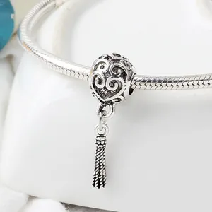Macro detail of hollow scrollwork silver bead charm with woven tassel on snake chain
