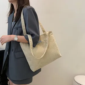 Detail view of beige corduroy tote bag showing ribbed texture and fashion label on model