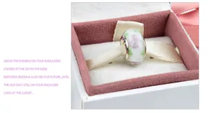 Macro view of a handmade milky white glass bead with pink floral patterns on pink velvet