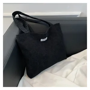 Macro detail of black corduroy tote bag with fashion label on a leather surface