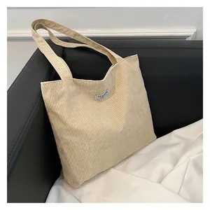 Close-up of beige corduroy tote bag showing ribbed texture and fashion label on the front