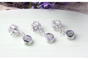 Close-up of three silver-tone zircon pendants on a decorative tray for bracelet making