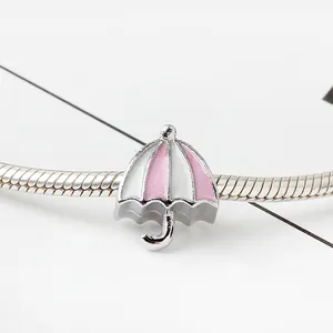 Detail macro-opname van een roze en witte emaille paraplu bedel aan een zilveren slangenarmband