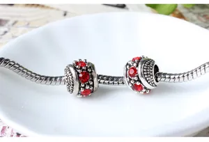 Macro shot of silver snake chain bracelet with two red rhinestone charms on white ceramic