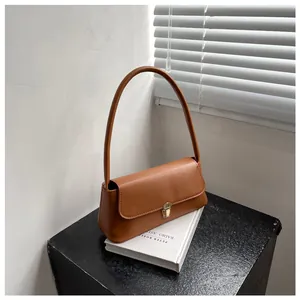Detailed close-up of a caramel brown baguette bag with golden buckle on white books