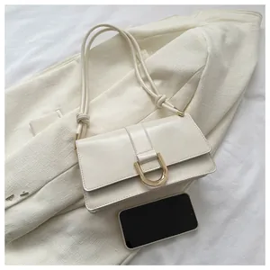 Close-up of cream shoulder bag with gold horseshoe buckle next to a smartphone