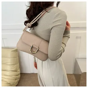 Detail of minimalist beige shoulder bag showing gold U-shaped hardware and fine leather texture