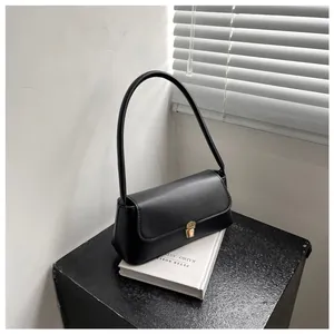 Detailed close-up of a black baguette shoulder bag with a gold metal push-lock closure