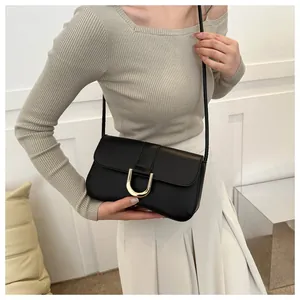 Detail of minimalist black leather underarm bag featuring a polished gold horseshoe buckle