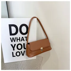 Detail of trendy brown baguette shoulder bag featuring a sleek golden metal lock closure
