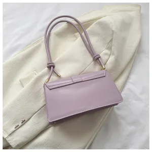 Detail of lavender shoulder bag with knotted strap and gold hardware on a tweed blazer