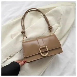 Close-up of khaki leather baguette bag featuring a large gold D-shaped buckle and knotted strap