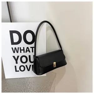 Detail of a black leather baguette bag with a golden square clasp on a minimal background