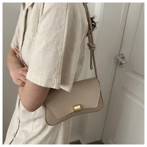 Close-up of beige baguette bag showing matte gold buckle and knotted shoulder strap detail