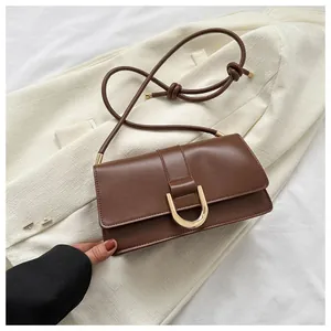 Detail of a brown rectangular crossbody bag with golden buckle on a white blazer