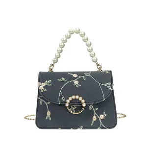 Sac à main broderie florale avec poignée en perles et chaîne dorée sur fond blanc