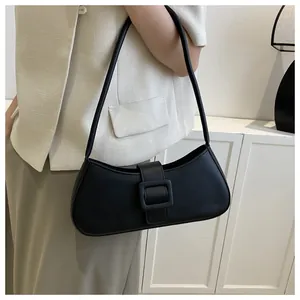 Detail view of the sleek black baguette bag with decorative buckle on a model shoulder