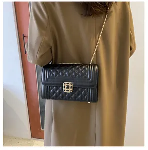 Detail of a black quilted crossbody bag with a gold chain strap and square lock clasp
