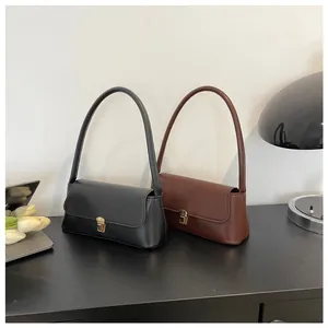 Minimalist black and brown shoulder bags with golden push-lock clasps on a modern desk