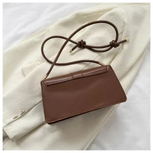 Close-up of brown rectangular shoulder bag with slim knotted strap and gold hardware