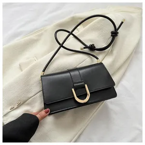 Detail of black leather bag with gold U-shaped buckle on beige blazer background