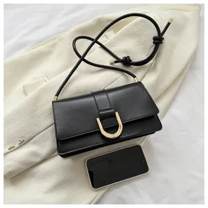 Detail of minimalist black leather flap bag featuring a striking gold U-shaped metal buckle