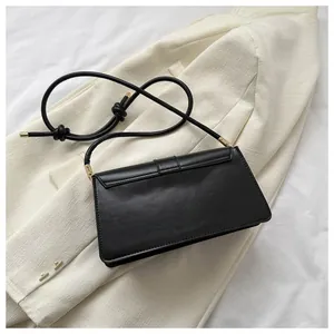 Detail of a matte black leather baguette bag on a beige blazer with gold hardware