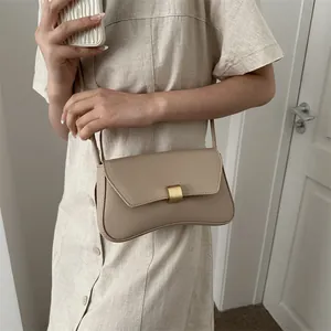 Chic beige underarm baguette bag with curved base and golden buckle on a model