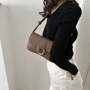 Brown leather baguette bag with gold U-shaped buckle styled on a black sweater