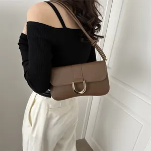 Detail of a brown leather shoulder bag with a gold D-ring buckle worn by a model