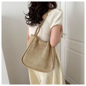 Dettaglio della borsa tote in paglia intrecciata con finiture in pelle indossata da modella