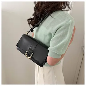 Close-up of a black baguette bag with gold horseshoe buckle on model with green sweater