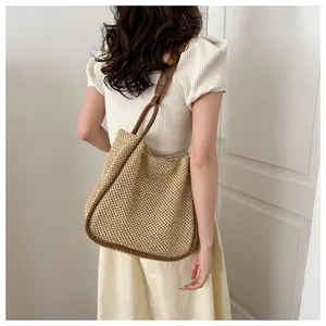 Grande borsa tote in paglia intrecciata con manici in pelle marrone indossata da una modella