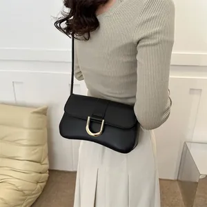 Minimalist black faux leather underarm bag with gold U-buckle worn by a model