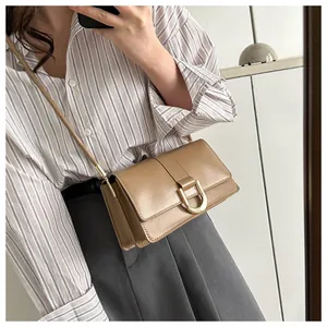 Brown leather crossbody baguette bag featuring a bold gold D-buckle on the front flap
