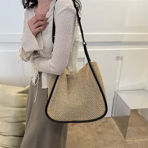Grande borsa tote in paglia con finiture in pelle nera indossata da una modella in casa