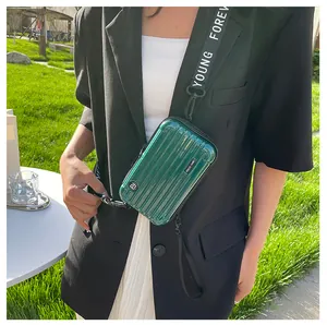 Dark green hardshell mini suitcase bag with Forever Young strap on grass