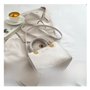 Detail of white crocodile texture handbag with woven handle and gold hardware accents