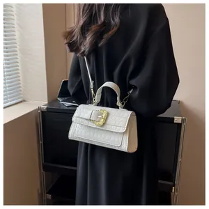 Close-up of white croc-embossed crossbody bag with gold baroque buckle on black dress