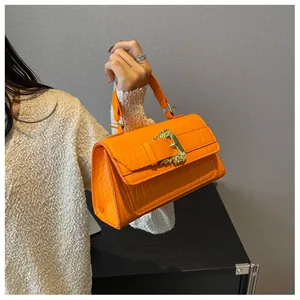 Detail of orange embossed leather handbag with golden relief buckle and flap closure