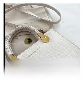 Detail of white crocodile pattern handbag with woven handle and gold hardware