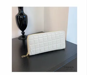 Detailed view of white quilted long wallet with golden zipper on a dark wooden table